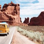 a yellow van on a road with a large rock formation in the background with Arches National Park in the background
