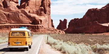 a yellow van on a road with a large rock formation in the background with Arches National Park in the background