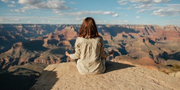 a woman sitting on a rock looking at a canyon