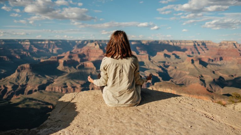 a woman sitting on a rock looking at a canyon